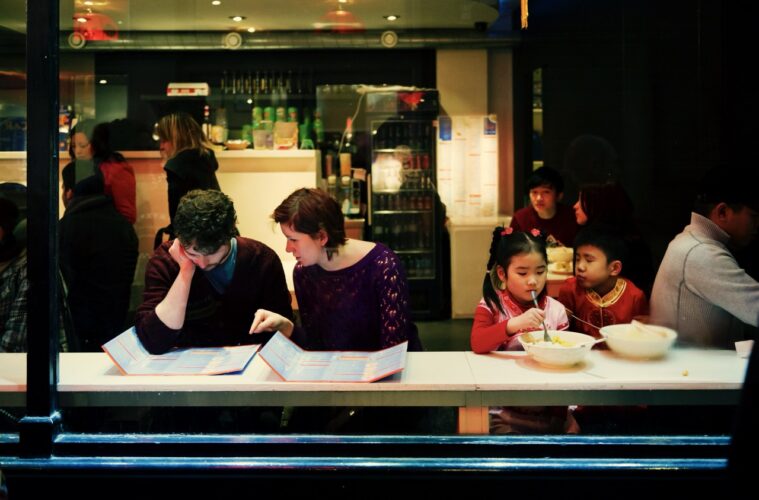 A cozy Shoreditch restaurant captured through the window, showing diners enjoying meals and browsing menus in a lively ambiance.