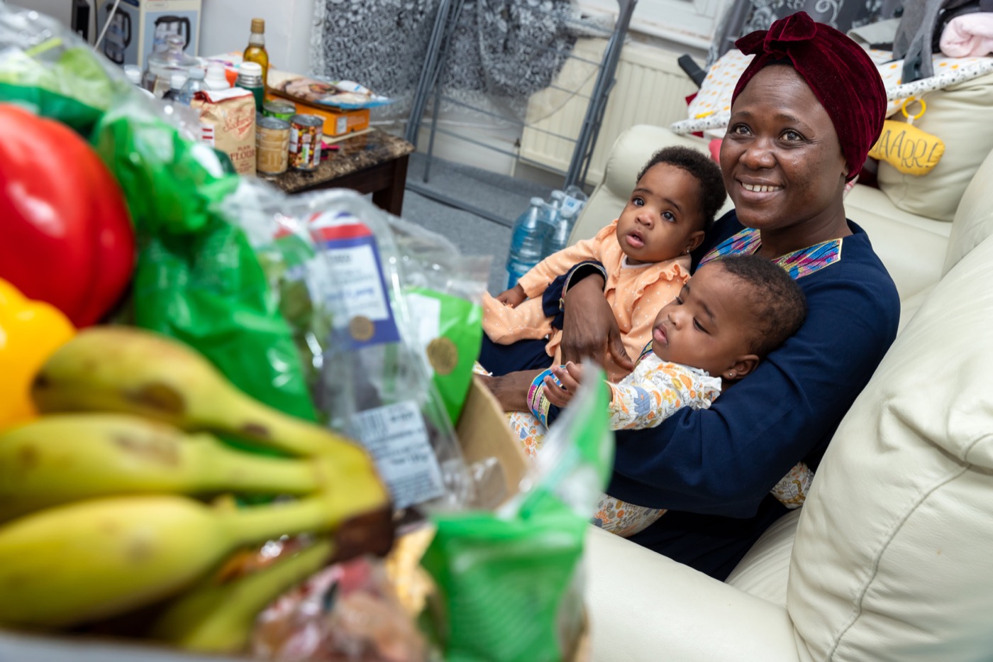 A joyful mother holding her two children surrounded by fresh produce, symbolizing the impact of the Feed London initiative.