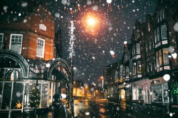 A magical snowfall illuminates a cozy Shoreditch street adorned with festive lights, capturing the spirit of Christmas.