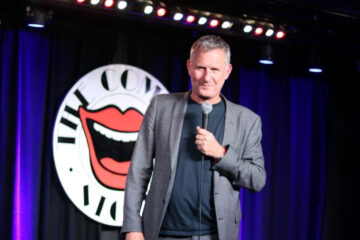 Comedian Adam Hills performing on stage at The Comedy Store, capturing the vibrant atmosphere of a comedy night in London.