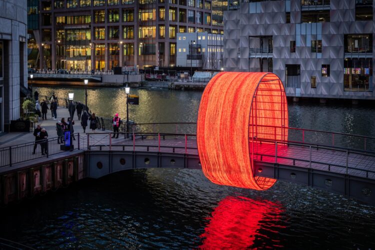 A glowing red light installation on a bridge at Canary Wharf Winter Lights, symbolizing creativity akin to The Lumineers’ new album Automatic.