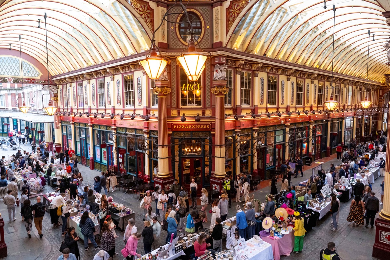 A bustling Leadenhall Market filled with vibrant stalls and shoppers, set against its iconic ornate architecture and glass roof.