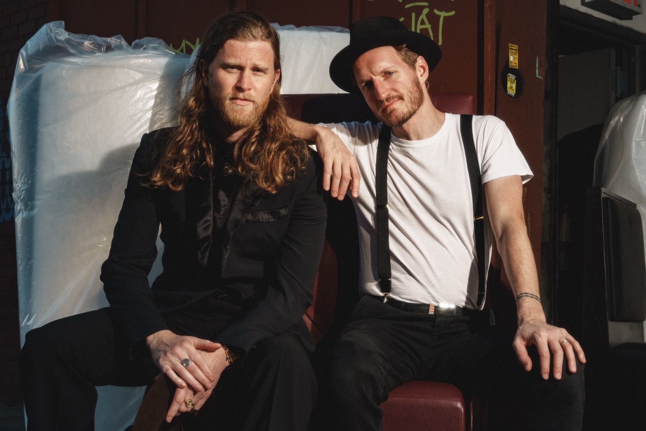 The Lumineers pose outdoors, exuding charm and style, promoting their new album Automatic with a confident and relaxed vibe.