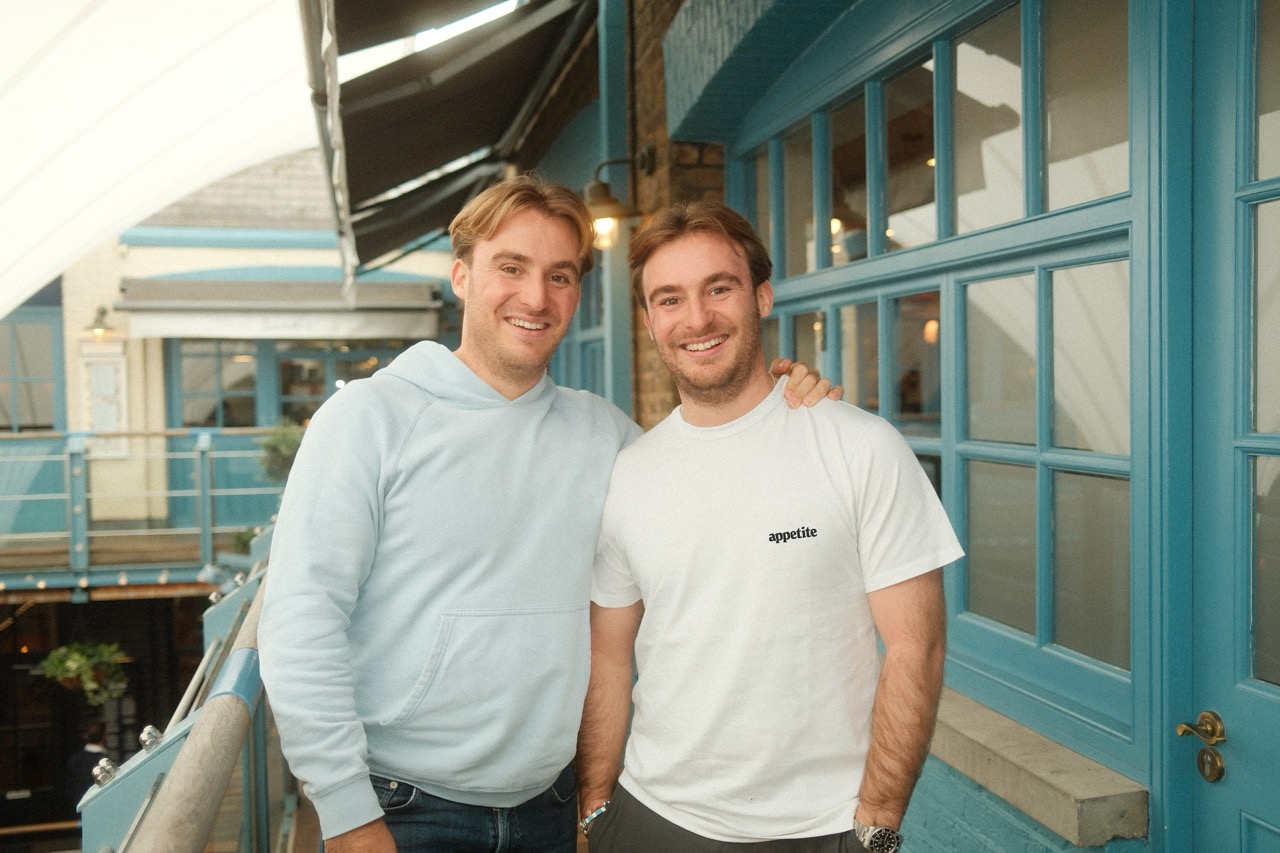 Toby & James Green, founders of Appetite, posing together outside a vibrant blue building, showcasing their entrepreneurial journey.