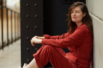 Madeleine Brettingham sitting casually in a red jumpsuit and white sneakers, exuding creative energy for Made in Shoreditch feature