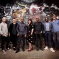 The Amy Winehouse Band poses against a graffiti-covered London wall, celebrating their legacy and upcoming tribute performance.