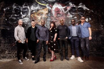 The Amy Winehouse Band poses against a graffiti-covered London wall, celebrating their legacy and upcoming tribute performance.