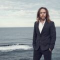 Tim Minchin stands against an ocean backdrop, bringing his signature wit and musical genius to the stage for his latest London show.