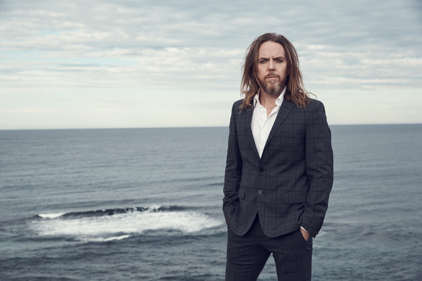 Tim Minchin stands against an ocean backdrop, bringing his signature wit and musical genius to the stage for his latest London show.