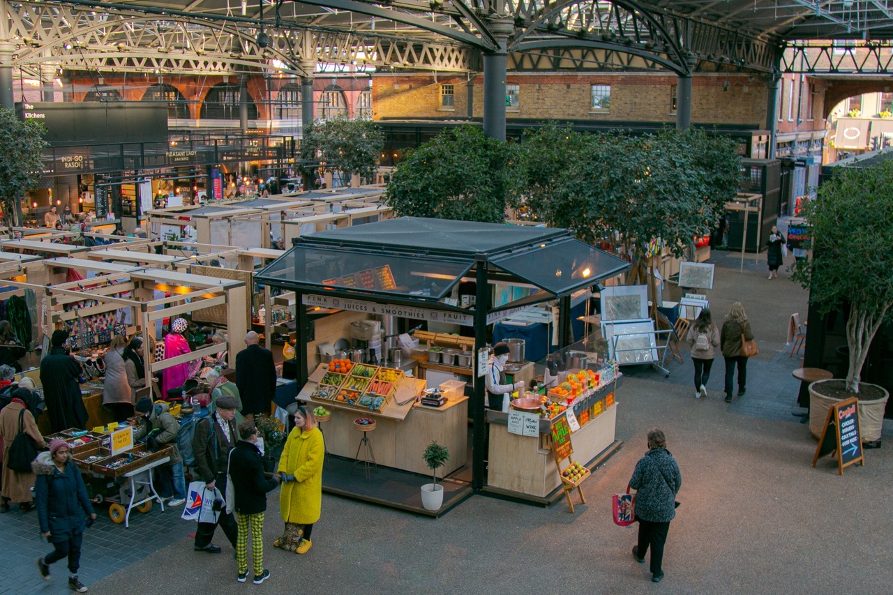 Bustling scene at Old Spitalfields Market in London, featuring artisan stalls, fresh produce, and vibrant shopping spots.