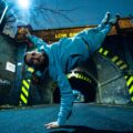 Dynamic breakdancer performing a gravity-defying move under a graffiti-covered tunnel at night, capturing the energy of Strictly Wandsworth.