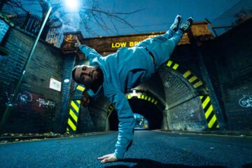 Dynamic breakdancer performing a gravity-defying move under a graffiti-covered tunnel at night, capturing the energy of Strictly Wandsworth.