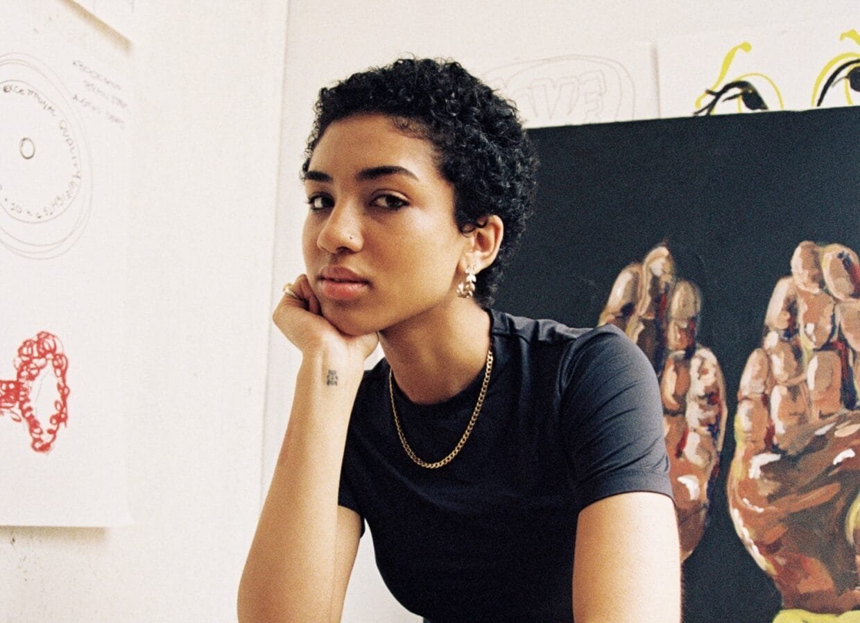 Artist Betty Ogun on Feminine Resilience and LOVE/FIGHT 6 Betty Ogun sitting beside artwork from LOVE/FIGHT exhibition