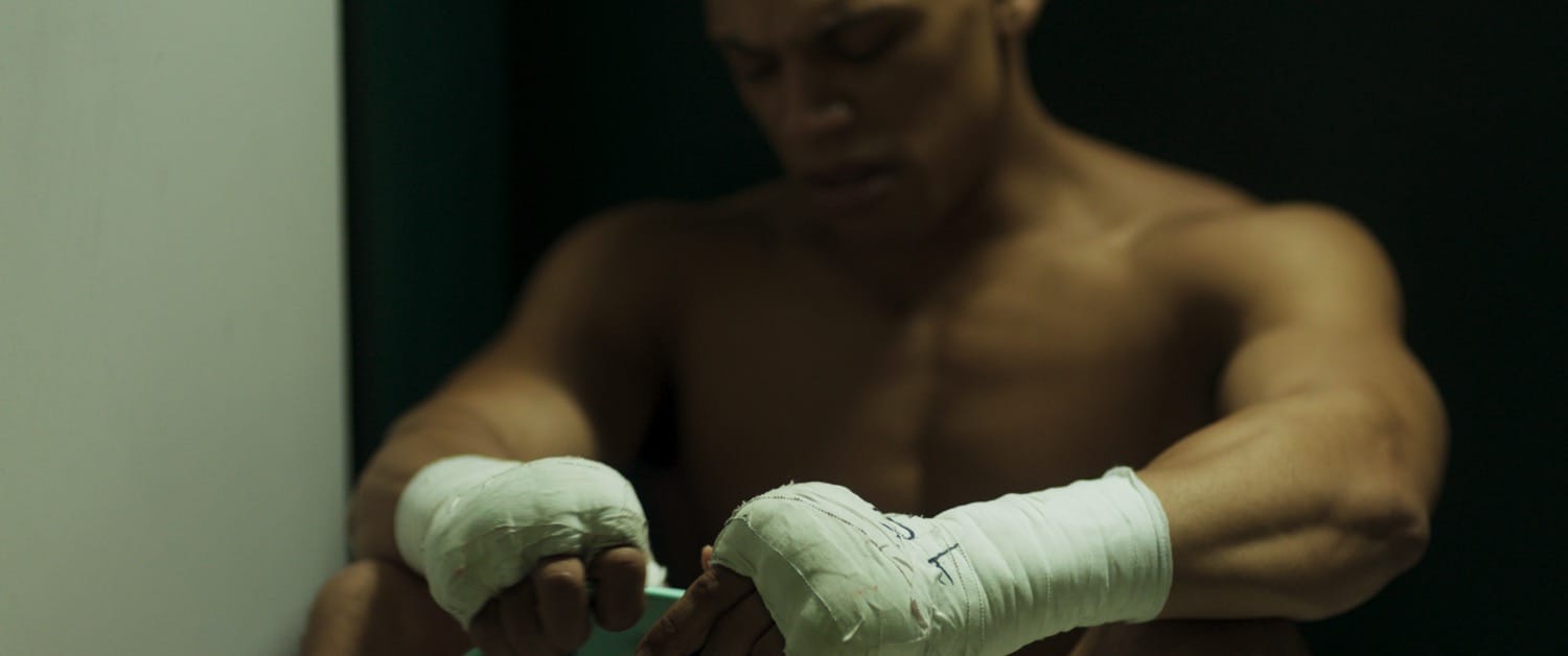 Close-up of taped hands under harsh fight-night lighting in HEAVYWEIGHT