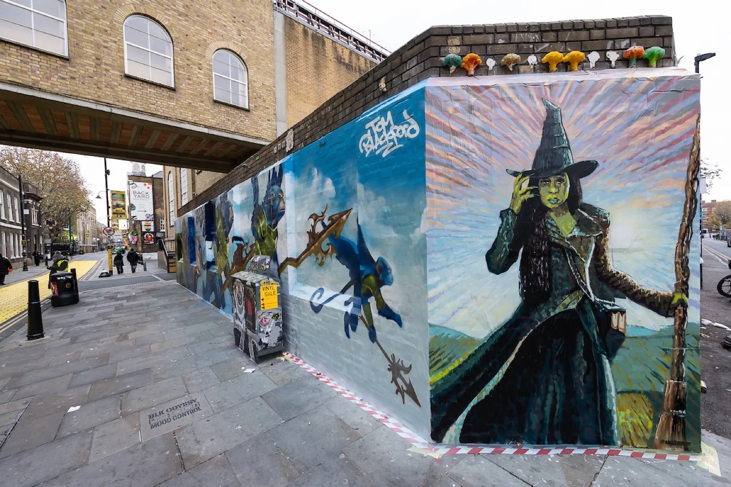 Mural on Brick Lane featuring Glinda and Elphaba, part of the Wicked Yellow Brick Lane street art transformation in East London.