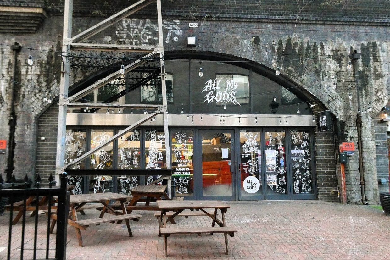 The front of All My Gods bar on Paradise Row in Bethnal Green, with benches outside a railway arch