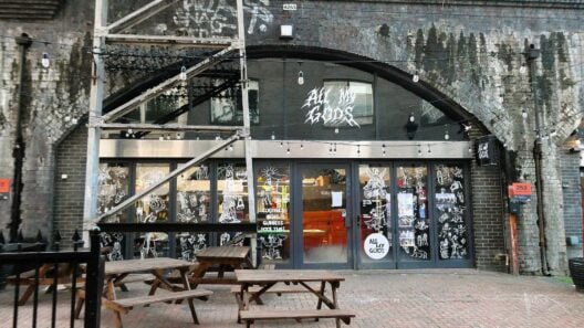 The front of All My Gods bar on Paradise Row in Bethnal Green, with benches outside a railway arch