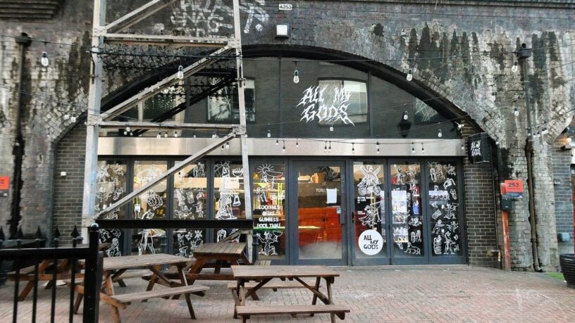 The front of All My Gods bar on Paradise Row in Bethnal Green, with benches outside a railway arch